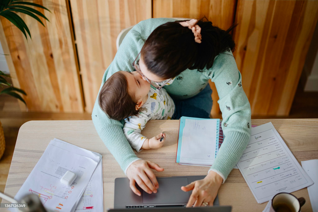 Mamma che lavora in scrivania e nel mentre da un bacio alla figlia