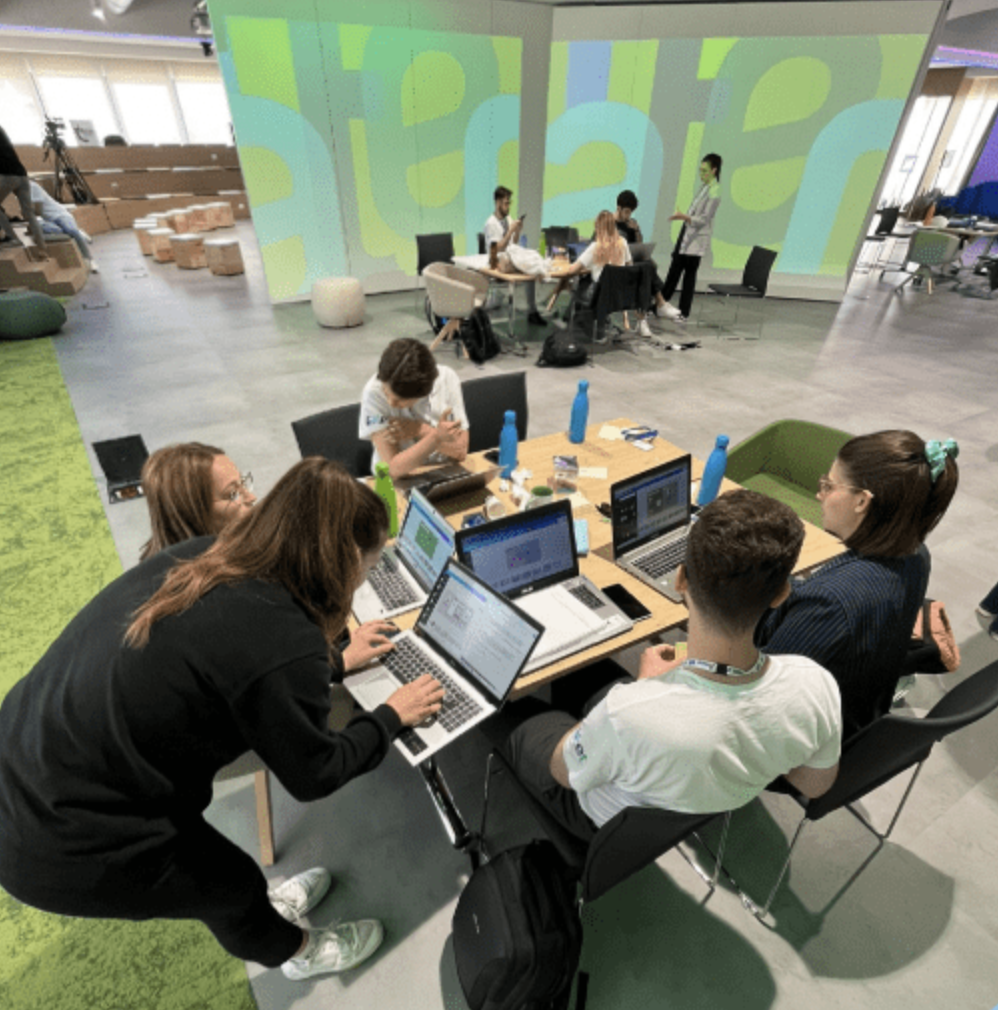 Un gruppo di giovani seduti in cerchio in uno spazio moderno e colorato lavora insieme a computer portatili.