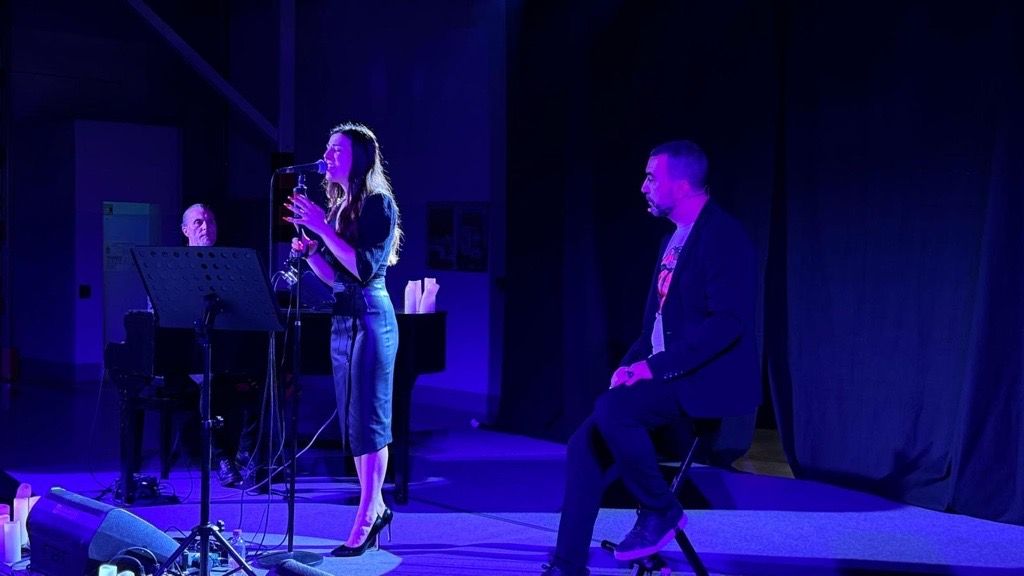 Due musicisti che suonano in un palco e a fianco il conduttore seduto.