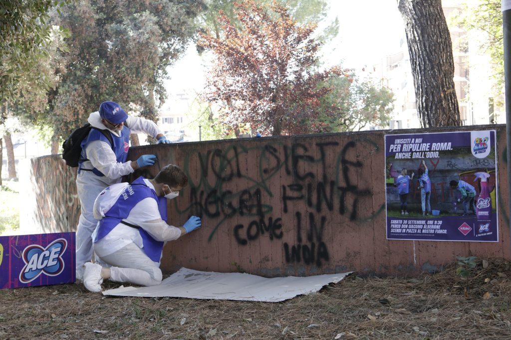 Volunteers in protective suits and gloves remove graffiti from a wall during an ACE activity.