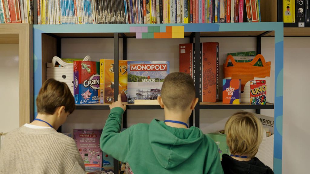 Two children look at a bookshelf filled with board games and colorful books.