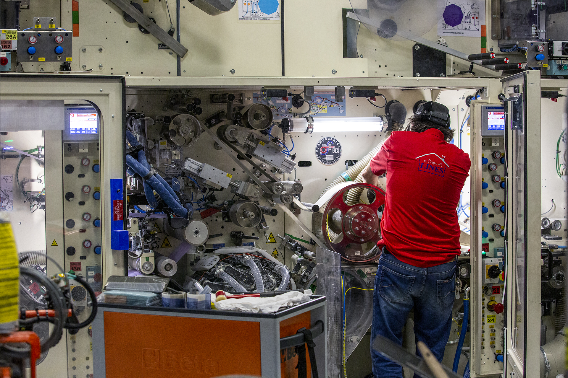 Tecnico in maglietta rossa al lavoro su un grande macchinario industriale con ingranaggi e tubi.