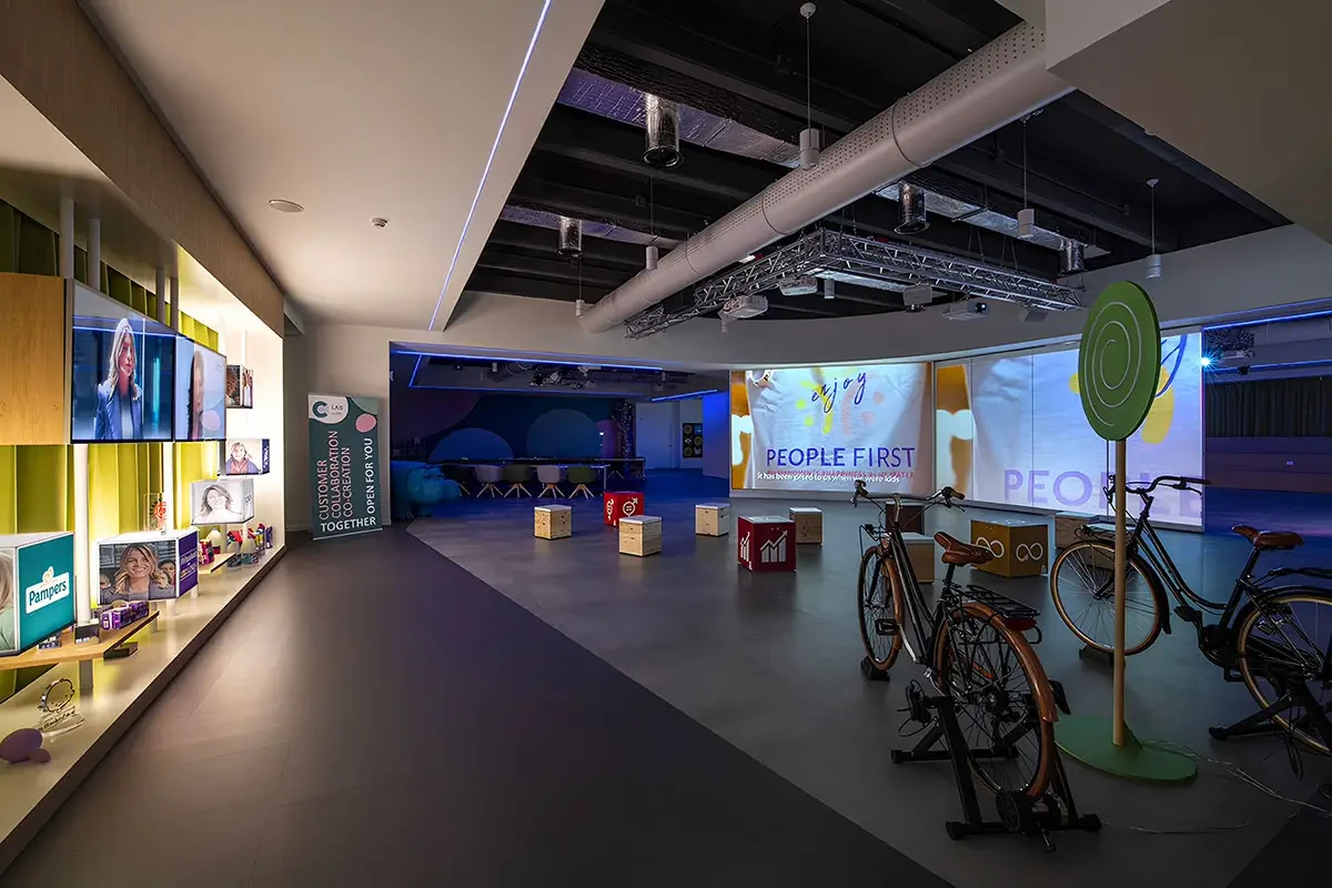 Un ampio spazio aziendale con proiezioni a parete sul tema People First, cubi decorativi e biciclette esposte.