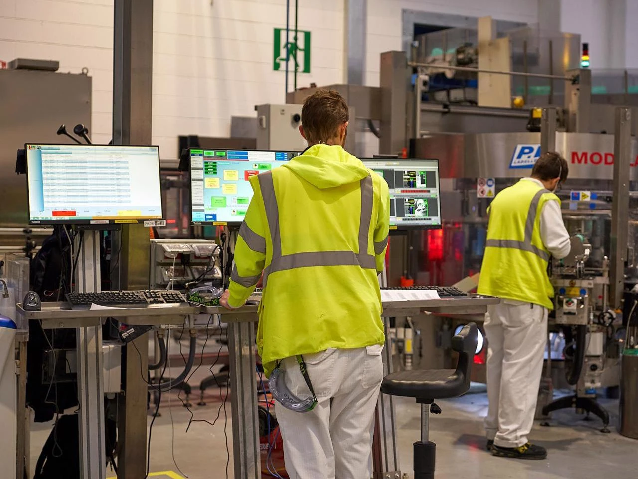 Operatore in giubbotto alta visibilità lavora davanti a monitor in fabbrica.